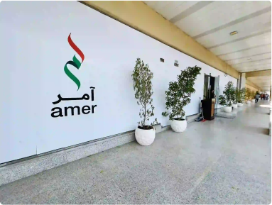 Exterior view of Amer Center entrance with logo and potted plants, 

showcasing facilities in Dubai.